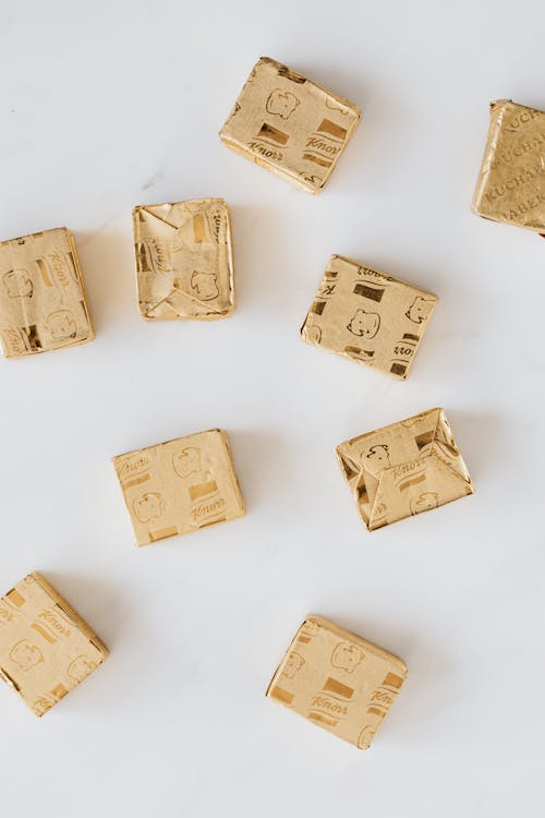 Top view of stock cubes in golden wrappers scattered on white marble table