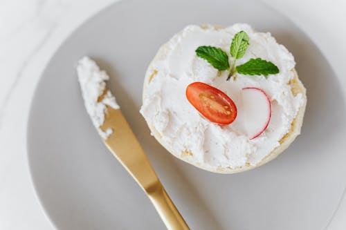 From above of delicious cottage cheese spread on bun decorated with vegetables and mint on round platter with golden knife placed on marble table