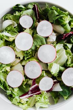 Overhead view of vegetarian salad with lettuce and purple cabbage decorated with radish slices in white bowl