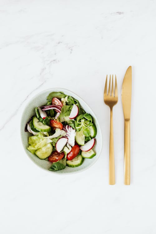 Delicious vegetable salad and golden fork and knife on table