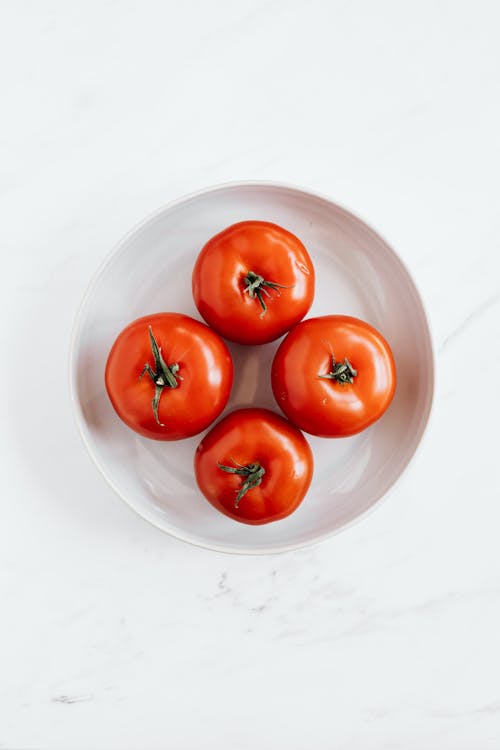 Ripe tomatoes in ceramic bowl placed on marble table