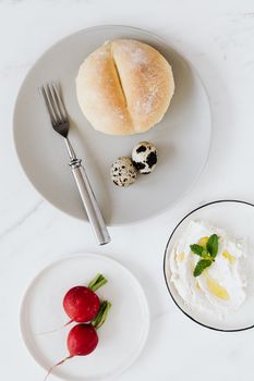 From above breakfast with bread cottage cheese quail eggs and radishes placed  on white plate biggest plate with fork
