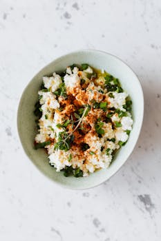 Top view of bowl with salad from cottage cheese green onion thyme and different spices placed on table in kitchen