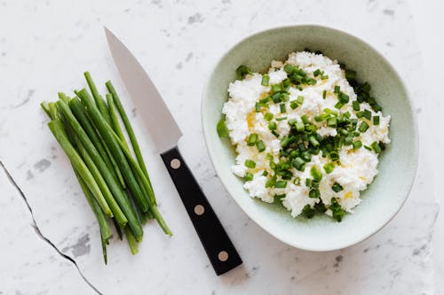 Top view of fresh salad with cottage cheese chopped onion oil and knife fresh greenery on white table with crack