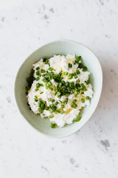 A top view of cottage cheese garnished with fresh green onions in a white bowl.