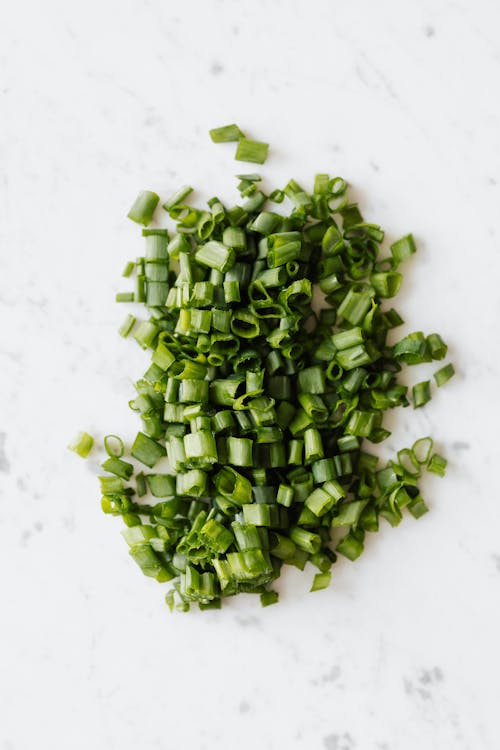 From above of fresh green onion chopped and prepared for vegetarian meal cooking on white table in kitchen
