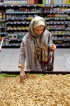 A Muslim woman in a hijab selecting peanuts in a grocery store aisle.