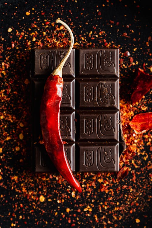 Top view of dry chili pepper placed on dark chocolate bar on dark table with ground spice