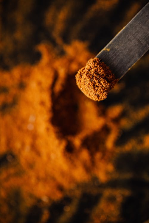 From above dark wooden spatula with sample of ground curcuma taken from heap