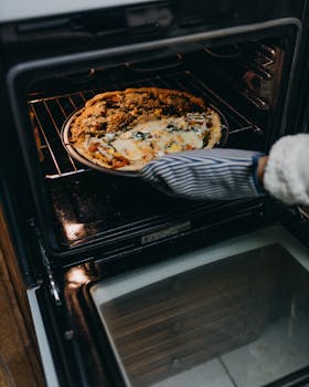 Freshly baked homemade pizza being taken out of the oven by a hand in a glove.