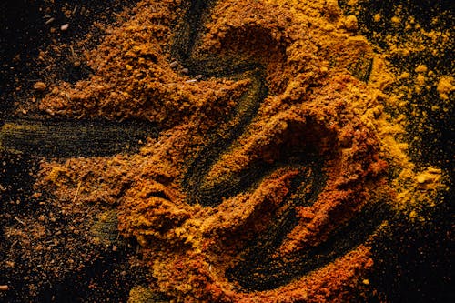Free From above of creative design of smoked ground paprika and turmeric mixed together on black surface Stock Photo