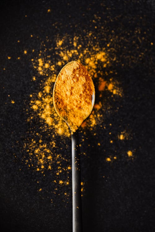 Free From above of creative composition of bright ground turmeric on metal tablespoon spilled on black table Stock Photo