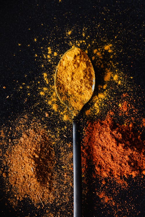 Top view of heap of powdered paprika and mix of peppers with bright curcuma in center on tablespoon on black background