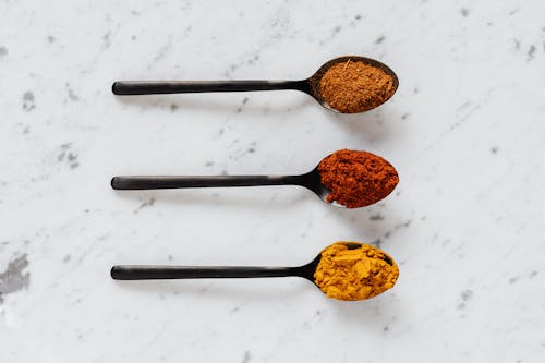 Free Top view of dry curcuma with smoked paprika and mix of ground peppers on plastic spoons on marble table Stock Photo