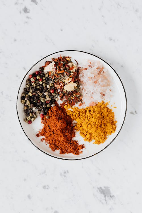 Free From above of bowl filled with piled of turmeric and paprika powder near mix of pepper flakes and seeds with sea salt on table Stock Photo