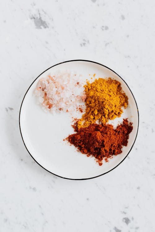 Free Top view of different powdered spices of curcuma and chili with pink salt in metal bowl on white marble surface Stock Photo