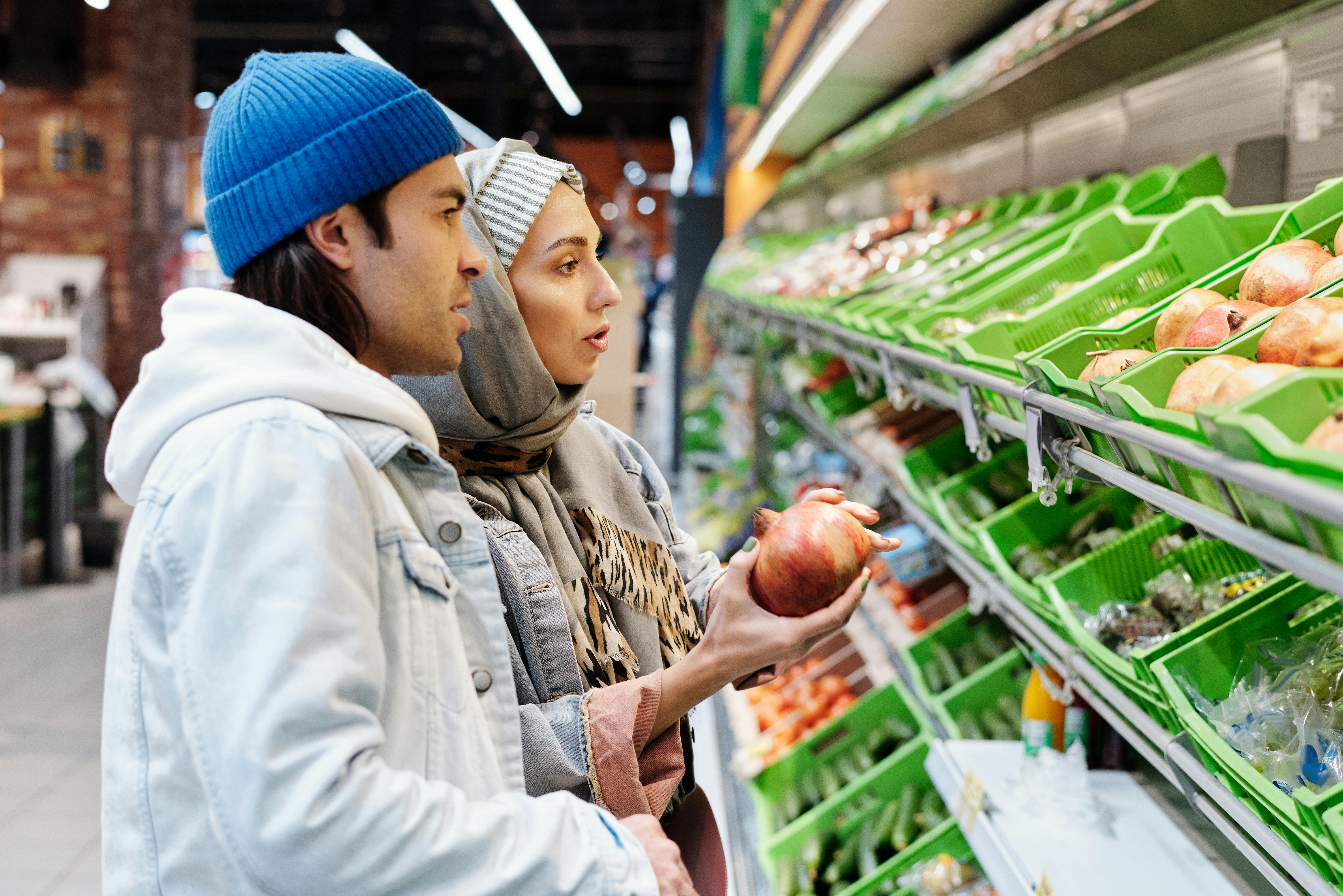 A couple selecting pomegranates in a grocery store aisle filled with fresh produce.