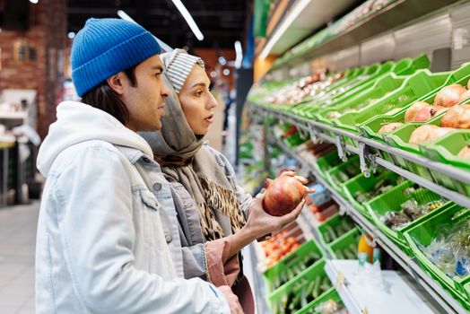 一对夫妇在杂货店的过道里挑选石榴，过道上摆满了新鲜的农产品