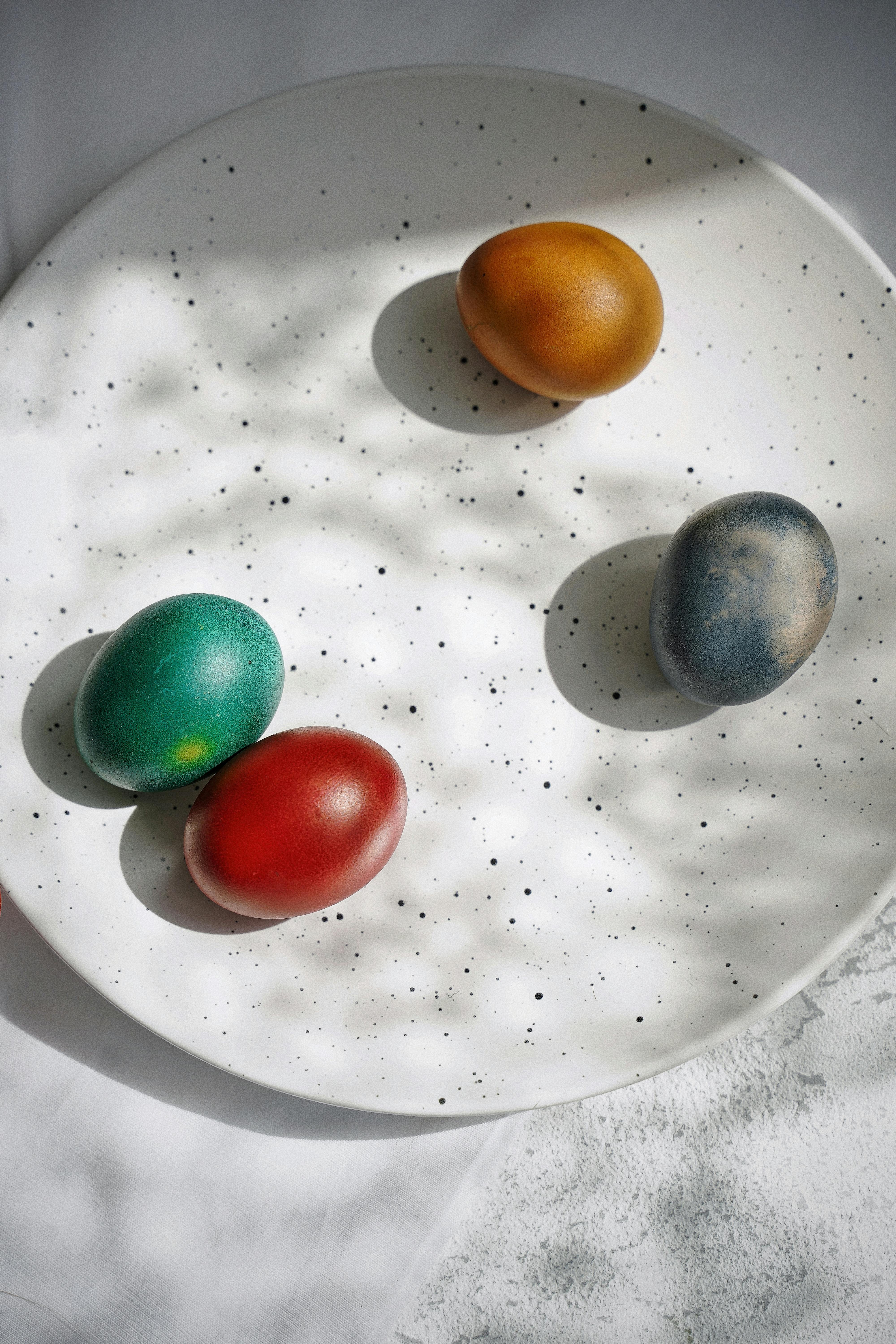 Colorful painted Easter eggs on a white speckled plate with shadows.