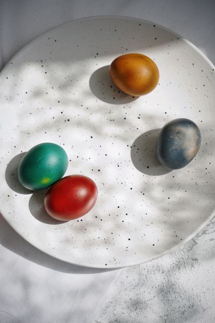 Colorful painted Easter eggs on a white speckled plate with shadows.