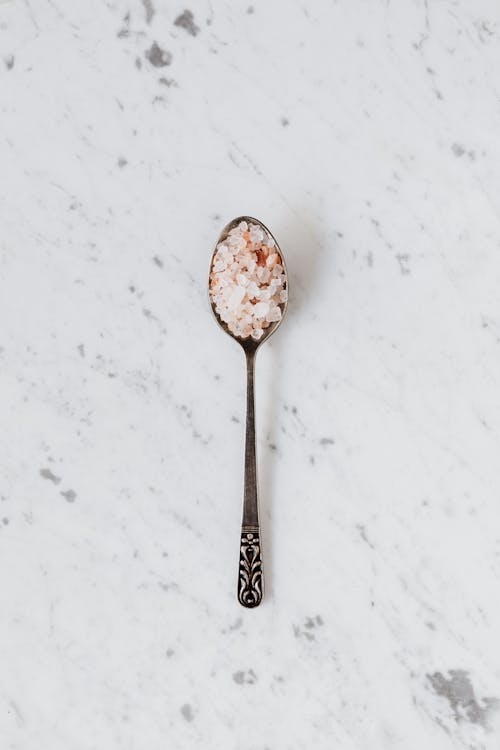 Top view of metal teaspoon with mix of salt and curcuma on smooth marble surface