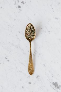 一个装有混合草药和香料的金属勺子，以顶视图放置在大理石台面上，用于健康美食的准备