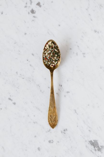 Top view of metal spoon filled with mixed herbs and spices used for healthy gourmet food preparing placed on marble surface