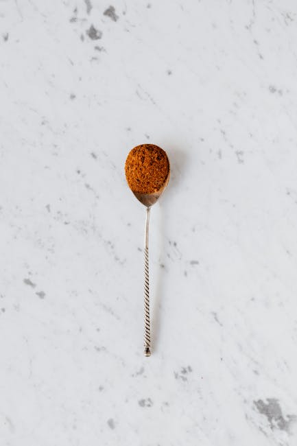 Top view of aromatic cinnamon condiment in vintage spoon used for baking and desserts placed on white marble surface