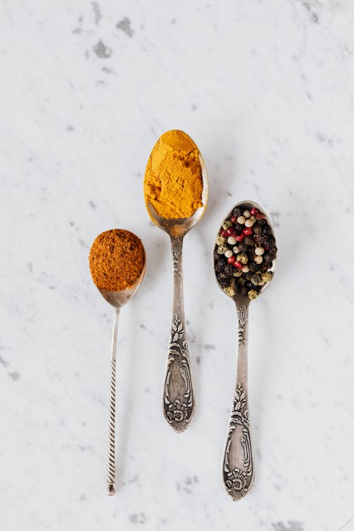 Top view composition with cinnamon and turmeric powder arranged on marble table together with mixed peppercorns used for gourmet and healthy food preparation