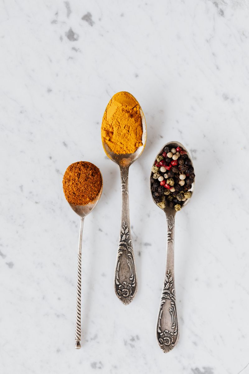 Turmeric powder and black peppercorns on vintage spoons