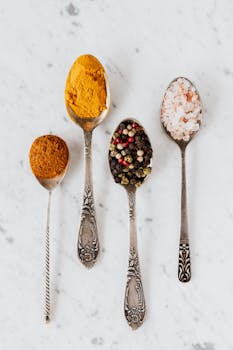 Top view of assorted spices and seasonings presented on vintage spoons over marble backdrop.