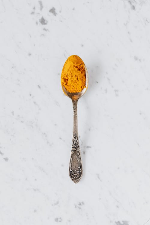 Free Top view of metal spoon with dry curcuma powder used for healthy gourmet food preparing placed on marble surface Stock Photo