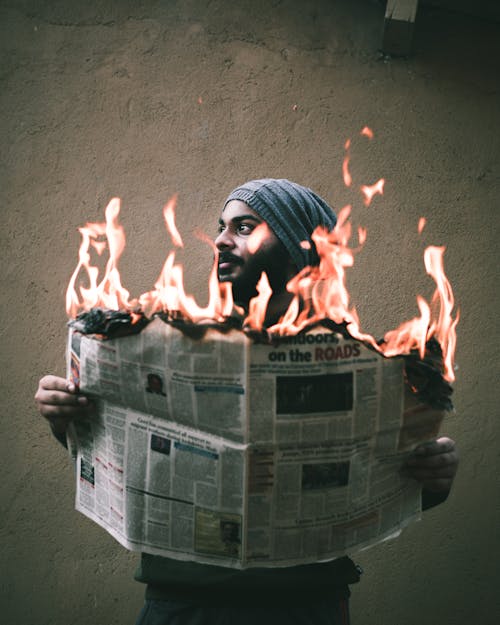 Bearded ethnic man burning newspaper near cement wall