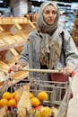 一位头戴头巾的女人在超市购物，她的购物车里装满了杂货和水果