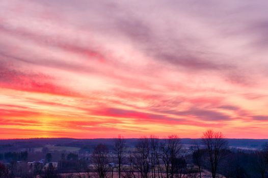 Low angle scenery view of colorful cloudy sky over leafless trees on hillside in wintertime at sunset