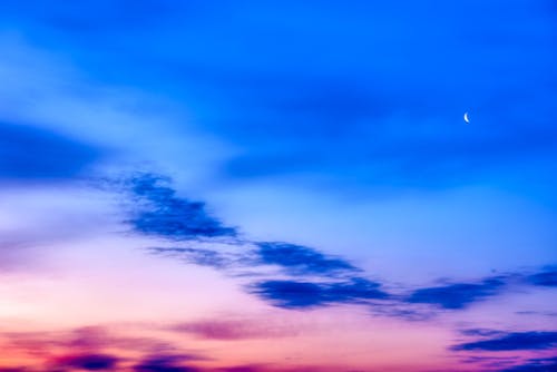 Picturesque bright cloudy sky with moon at sundown