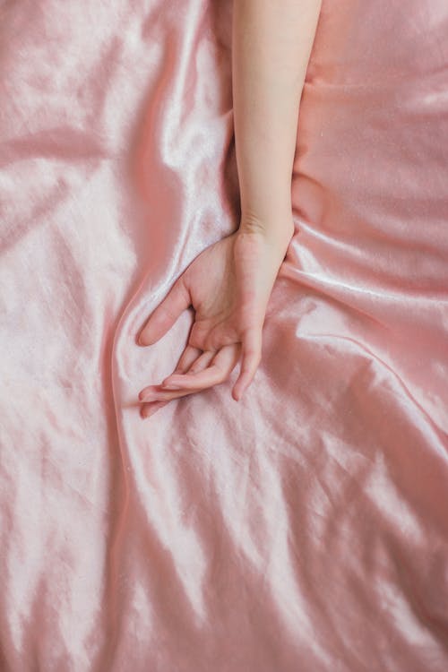 Top view of hand of crop anonymous female on soft silk creased bed sheet at home