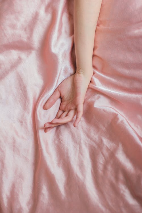 Free Top view of hand of crop anonymous female on soft silk creased bed sheet at home Stock Photo