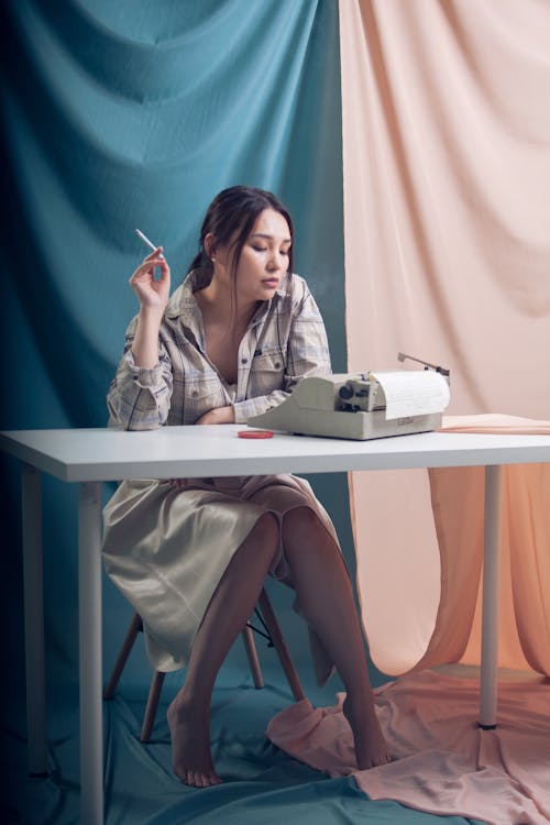 Stylish woman with cigarette sitting at table with retro typewriter