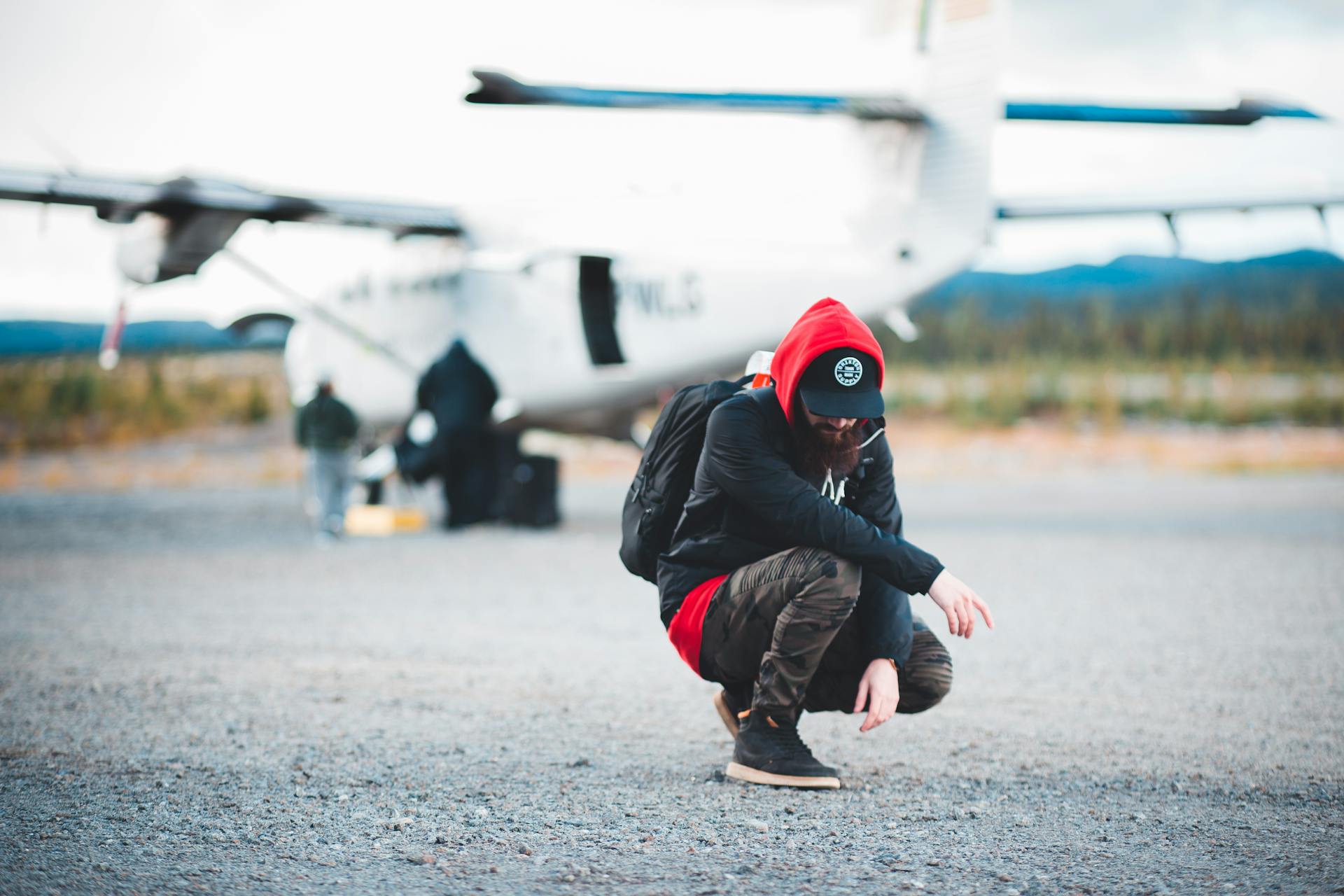 A modern traveler crouches by a private plane on an airfield, showcasing a blend of adventure and style.