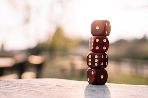 Set of red dice stacked together on wooden table placed on sunny terrace in daylight