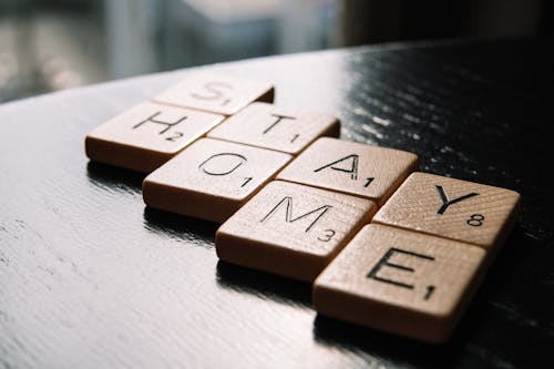 High angle of scrabble letter tiles arranged on black wooden table in inscription Stay Home in living room