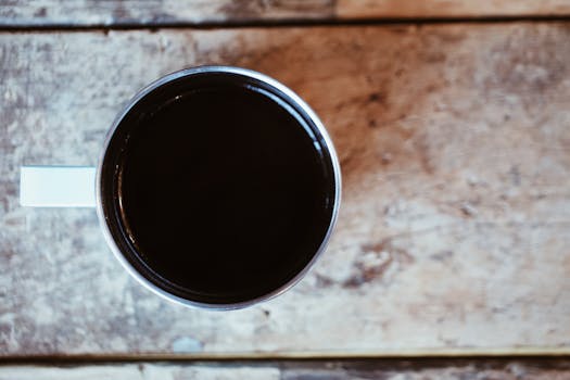 Top view of white cup of aromatic freshly brewed coffee placed on wooden weathered table