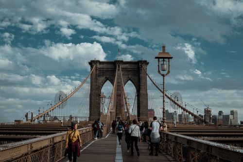 Free People walking on Brooklyn Bridge with a view of the Manhattan skyline under a cloudy sky. Stock Photo
