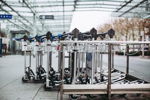 Row of luggage carts lined up outdoors at an airport terminal on a clear day.