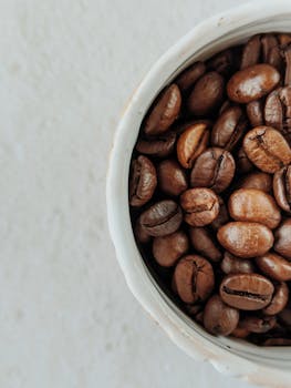 Macro shot of roasted coffee beans in a white ceramic cup, perfect for coffee lovers.