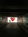 Side view of person silhouette walking across paved underground pedestrian passage with graffiti on walls