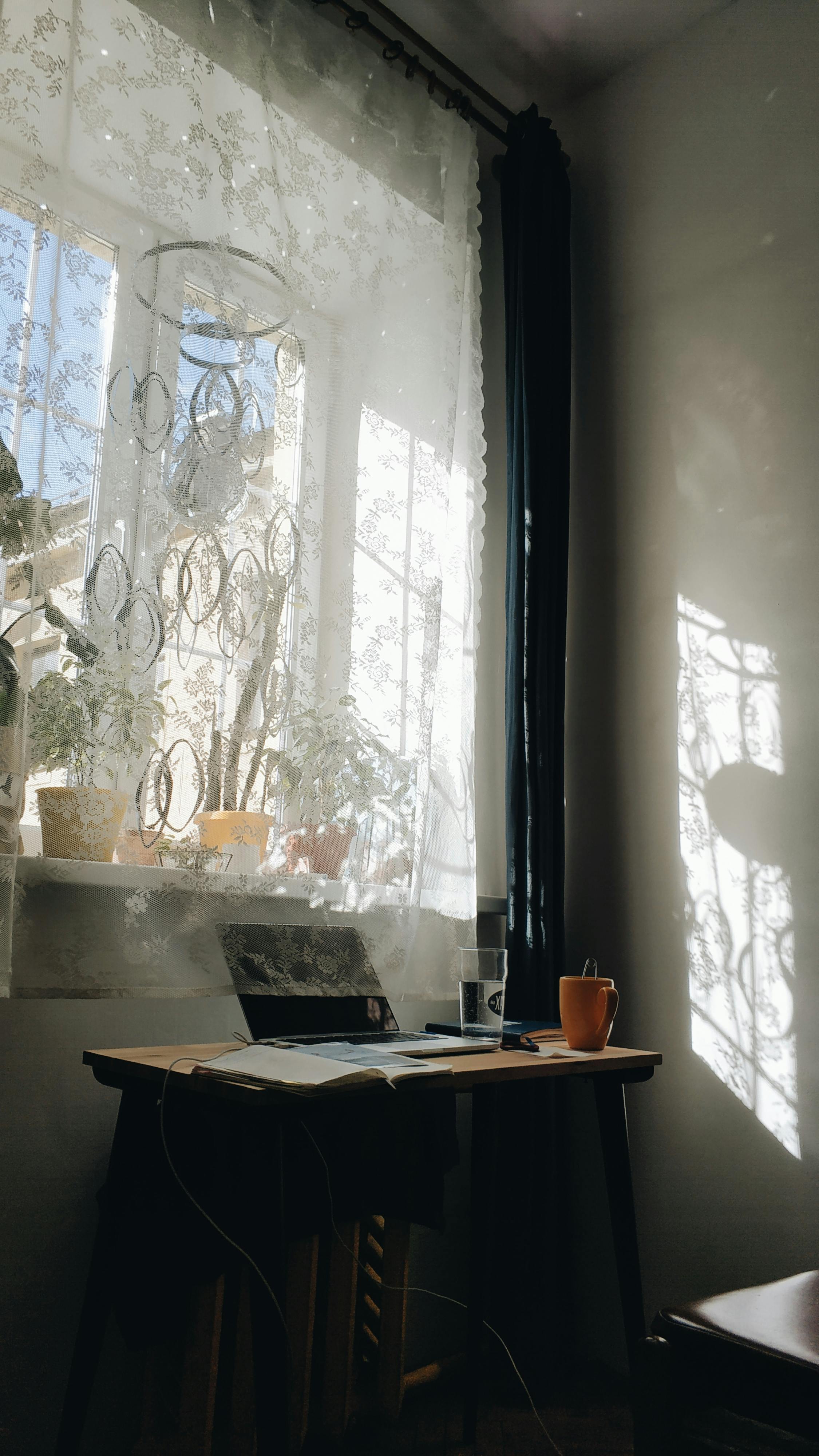 Free Serene home office with sunlight streaming through a window, highlighting a desk with a coffee cup. Stock Photo