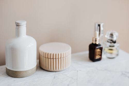 Refillable cosmetic containers arranged on a white marble bathroom shelf