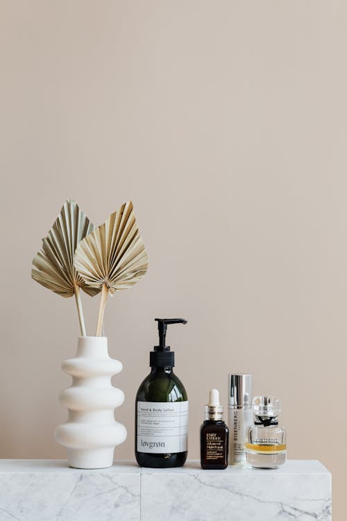 Set of cosmetic supplies near decorative leaves in vase on marble shelf